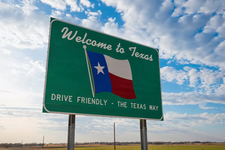 Green road sign with "Welcome to Texas" above Texas flag and "Drive Friendly - the Texas Way" below.